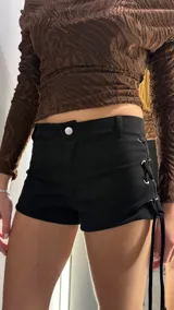 Short negro de gamuza con diseño de cordones cruzados en los laterales y ojales metálicos plateados. Presenta un corte ajustado y tiro bajo.