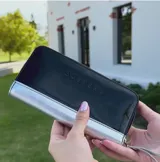 Billetera mediana de cuero color negro con detalle plateado en la parte inferior y cierre perimetral.