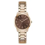 Reloj analógico Guess modelo Winni con caja y malla de acero inoxidable en tono oro rosa. Presenta una esfera redonda de color marrón con acabado sunray, números arábigos en las posiciones 3, 6, 9 y 12, y un diseño de eslabones hexagonales en la pulsera.