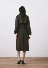 Chaqueta estilo gabardina larga en color gris oscuro, con doble botonadura frontal, solapas clásicas, bolsillos y trabillas ajustables en los puños.