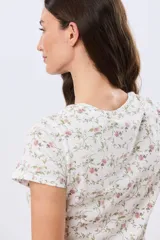 Remera de manga corta con cuello redondo, confeccionada en algodón con estampa de diseño floral en tonos rosados y verdes sobre base beige.