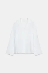 Camisa blanca de lino 100% con cuello solapa de muescas, manga larga y bajo asimétrico. Cierre frontal con botones.