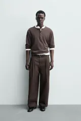 Pantalón chino de corte wide fit confeccionado en tejido de algodón. Presenta pliegues frontales, bolsillos laterales y bolsillos traseros de vivo, con cierre frontal de cremallera y botón.