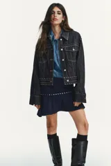 Falda corta azul marino de tiro medio, con detalle de tachas plateadas y bajo con volante asimétrico. Cierre lateral con cremallera oculta.