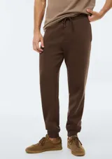 Pantalón de jogging tipo babucha color marrón, confeccionado con felpa, con cordones ajustables en la cintura y puños elásticos en los tobillos.
