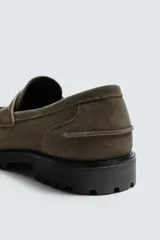 Mocasín de vestir en piel con acabado serraje color verde militar, con detalle de antifaz en el empeine y suela track dentada.