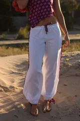 Pantalon de lino color blanco, de corte holgado y estilo babucha, con detalles de franjas estampadas en los laterales y cordones ajustables en los tobillos.