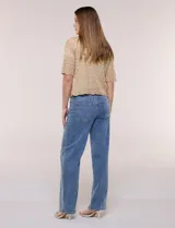 Bolero corto de punto beige, con diseño abierto sin botones y mangas cortas. Presenta un patrón de tejido calado con detalles geométricos y terminaciones onduladas en los bordes.