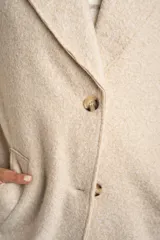 Tapado largo color beige claro, de corte oversize, con cuello solapa y cierre frontal de botones.