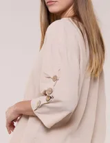 Blusa Erika de algodón con estampado de rayas en tonos azules, rosados y amarillos. Presenta cuello redondo con escote en V y botones frontales, mangas cortas decoradas con una fila de botones en los laterales y dobladillo asimétrico.