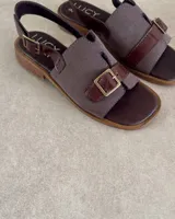 Sandalias marrones con tiras anchas de tela y cuero sintético, hebilla metálica y suela plana.