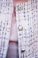 Chaqueta corta tipo Chanel de tweed color rosa, con botones fantasía y cuello redondo.