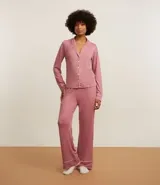 Conjunto de pijama americano largo color rosa, compuesto por camisa de manga larga con cuello solapa, abotonado delantero y pantalón con cintura elástica. Ambas prendas tienen detalles de vivos y botones contrastantes en color blanco.