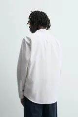 Camisa de manga larga, color blanco, con cuello italiano y corte slim fit. Presenta cierre frontal de botonadura y puños con botón.