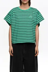 Remera corta de corte amplio confeccionada en 100% algodón, con diseño a rayas horizontales azules y negras, escote redondo, mangas cortas caídas y pequeño logo bordado en el pecho.
