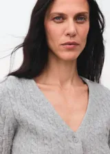 Cardigan de punto trenzado en color gris, con cuello en pico, manga larga y cierre frontal con botones.