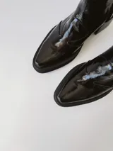 Botas texanas negras de cuero charol con caña baja, punta fina y tacón cuadrado.