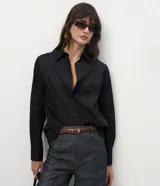 Camisa básica de mujer confeccionada en tricolina de algodón, con cuello solapa, cierre frontal de botones y mangas largas con puños abotonados.