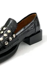 Mocasín de cuero charol negro con detalle de apliques metálicos plateados en la parte delantera y taco bajo cuadrado.