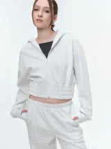 Campera deportiva cropped con capucha y cierre frontal, color gris melange. Presenta cintura y puños elastizados, diseño de manga larga y bolsillos frontales.