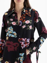 Camisa de seda color blanco con estampado floral y de dragones en tonos rojos, azules y verdes. Tiene cuello clásico, mangas largas con puños ajustables y botones forrados.