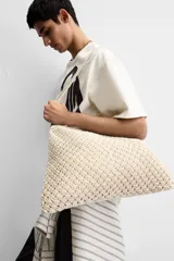Bolso tipo shopper color crudo, confeccionado en tejido trenzado de algodón con diseño de macramé. Cuenta con dos asas de hombro ajustables que funcionan como cierre del compartimento principal.