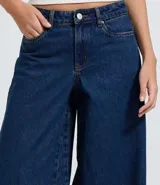 Pantalón de jean azul oscuro con corte super wide leg, cintura media, bolsillos funcionales y ruedo deshilachado.