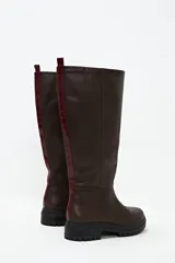 Bota de cuero color chocolate, de caña alta y suela track. Presenta detalle de textura símil cocodrilo en la parte trasera de la caña.