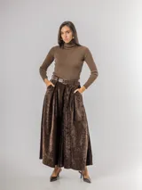 Pantalón tipo palazzo de corte amplio y tiro alto, confeccionado en tela aterciopelada color marrón chocolate. Presenta pinzas en la cintura, bolsillos laterales y cierre con cinturón de cuero marrón incluido.