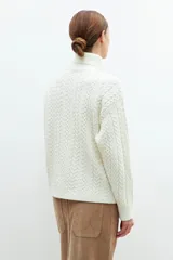 Polera color crudo con cuello alto y tejido con diseño de trenzas.