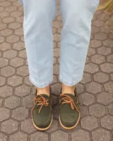 Zapatos náuticos de cuero verde oscuro, estilo mocasín con cordones de cuero marrón claro, costuras visibles en contraste y suela plana.
