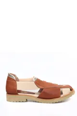Zapato tipo sandalia plana con diseño de tiras en cuero color marrón y paneles elásticos en color crema. Presenta suela dentada de goma y detalle de refuerzo metalizado en el talón.