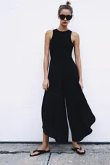 Mono largo negro con cuerpo de tejido ajustado sin mangas y cuello redondo, combinado con pantalón ancho de tejido fluido y satinado con diseño abullonado y bajo asimétrico. Cierre trasero con cremallera oculta.