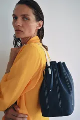 Bolso de hombro tipo saco confeccionado en piel azul marino, con detalle de pespuntes blancos verticales, asas finas de hombro en color blanco y cierre fruncido.