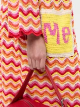 Saco tejido largo con diseño de ondas en tonos naranja, rosa, amarillo y blanco. Tiene bolsillos delanteros y mangas largas acampanadas.