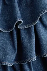 Pollera mini de denim de algodón rígido, con diseño de triple capa de volados escalonados.