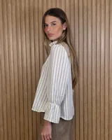 Blusa color lila con estampado vertical de ramas y hojas blancas, cuello alto con volados y escote en V. Presenta mangas largas abullonadas con puños elastizados.