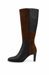 Bota alta bicolor con diseño de paneles en combinación de cuero negro y gamuza marrón. Cuenta con punta cuadrada suave, caña recta alta y taco fino.