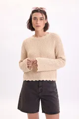 Sweater de punto fantasía con lurex en color beige, cuello redondo y mangas largas con terminaciones en ondas.