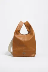 Bolso de mano Bimba y Lola modelo Paper mediano, confeccionado en cuero color tostado con estructura blanda, asas superiores y correa de hombro ajustable en color beige. Presenta costuras visibles, logo metálico de la marca en la parte inferior y cierre principal.