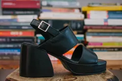 Sandalias de cuero negro con plataforma y tacón ancho de madera. Tiras anchas sobre el empeine y tobillo con hebilla metálica.