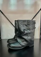 Botas de caña baja color negro, con diseño holgado y dos correas decorativas con hebillas metálicas en la parte superior.