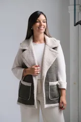 Chaleco de gamuza sintética en color verde oliva con interior y bordes de corderito beige. Presenta solapas amplias, dos bolsillos frontales aplicados y un diseño abierto sin cierre.
