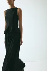 Top sin mangas con escote bote, costuras moldeadoras y pliegues en la cintura que forman un peplum acampanado. Cuenta con cierre oculto en la espalda y diseño de corte sastre en color negro.