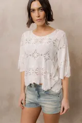 Blusa de punto calado color blanco, con diseño geométrico y floral transparente, escote redondo y mangas tres cuartos amplias de calce relajado.