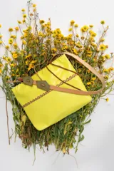 Cartera bandolera de cuero flexible color amarillo, con trenza artesanal al frente, interior forrado y correa larga con herrajes de metal.
