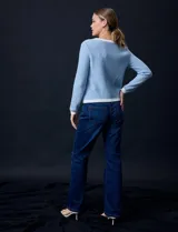 Cardigan de tejido tweed celeste y blanco, con escote redondo, cierre frontal con botones metálicos dorados y bolsillos simulados en el frente.