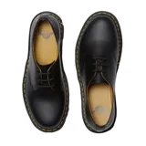 Zapato de cuero negro con cordones, diseño clásico de tres ojales, suela de goma con cámara de aire y costuras amarillas distintivas en el borde.