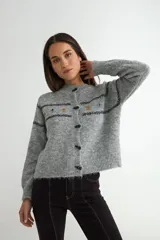 Cardigan de punto gris con cierre frontal de botones oscuros. Presenta un diseño de rayas horizontales oscuras y pequeños bordados florales en la parte superior del pecho y mangas.
