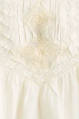 Top de algodón color beige claro con cuello de volados, canesú en V con jaretas y detalles bordados al frente, y mangas circulares con volados.